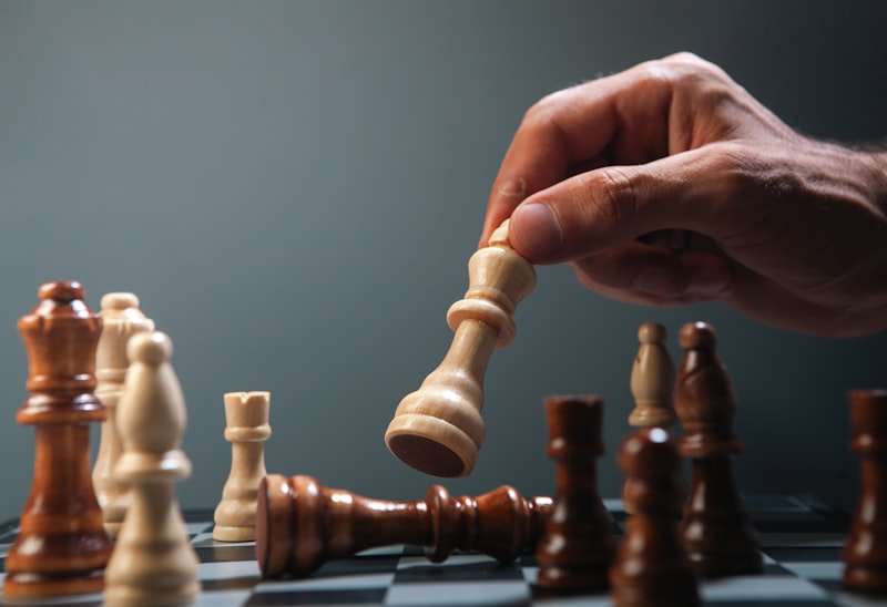 Hand moving a white chess piece over fallen king.